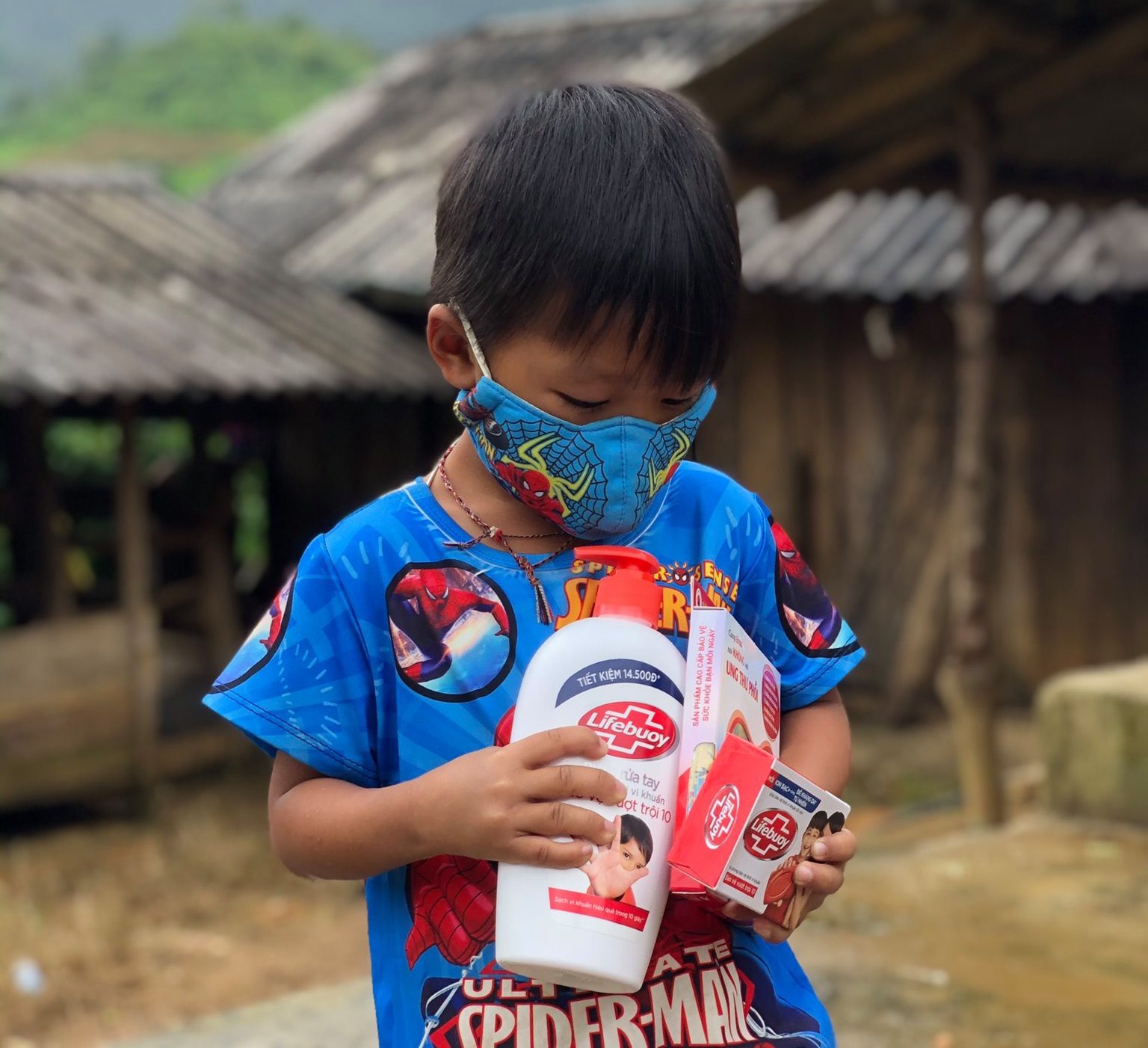 A boy holds hand sanitizer and masks that he received in his COVID prevention kit from Helen Keller.