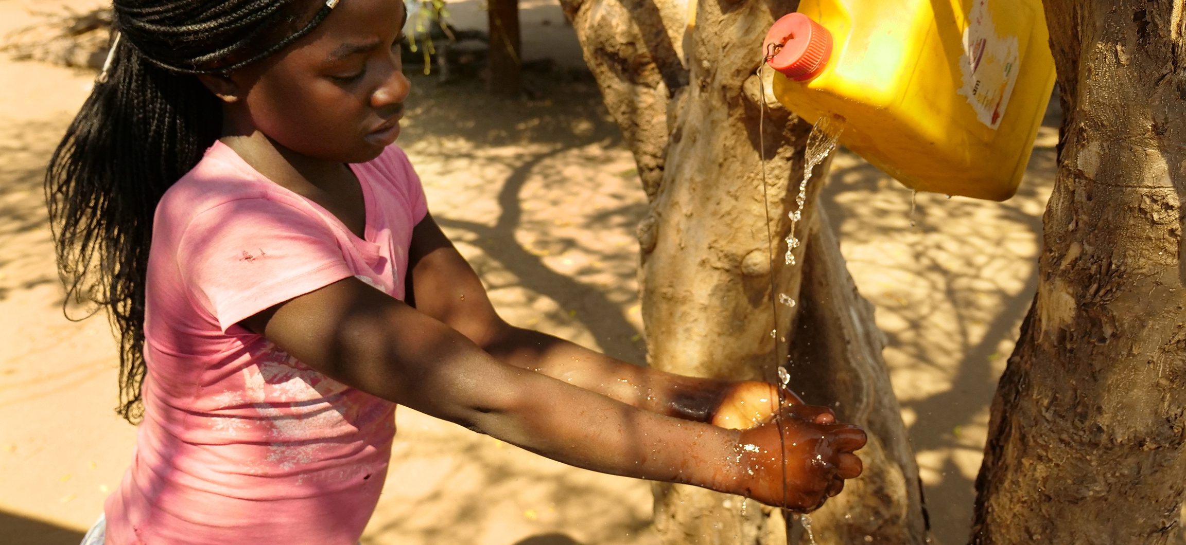 A young girl uses a hands-free device to pour water for washing her hands.