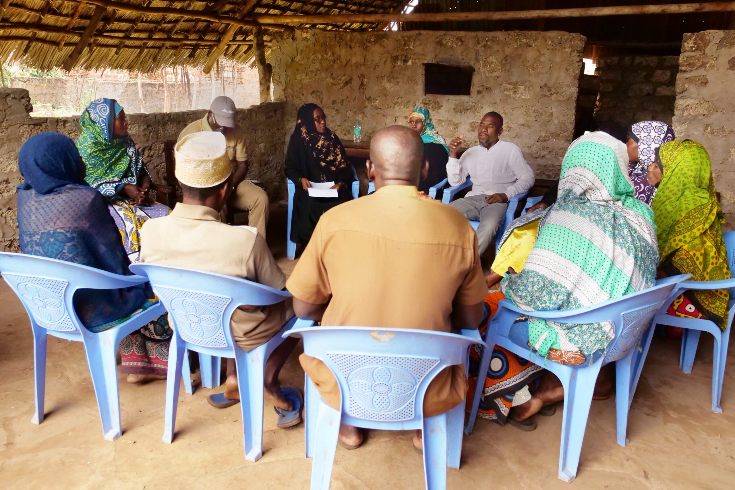 Community members sit in a circle of plastic chairs, participating in a community dialogue led by Sharmilla