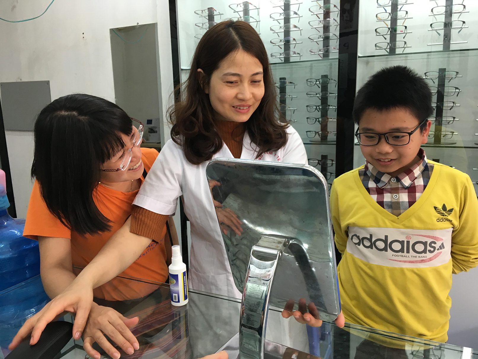 Ngoc looks on as an optician helps a boy choose eye glasses that will not only help him see, but that he will also be proud to wear
