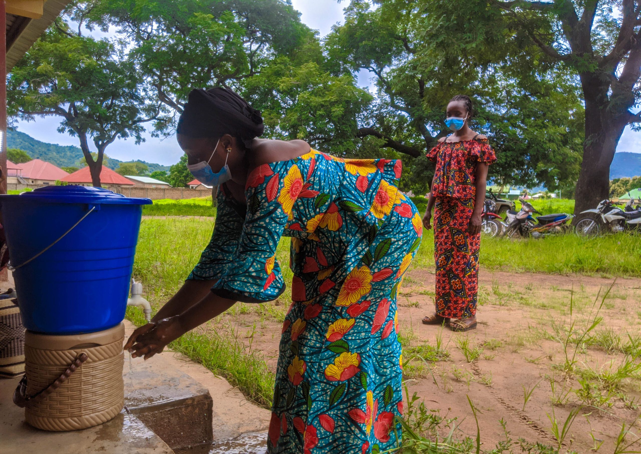 A woman washes her hands using a spout from a small bucket of water.