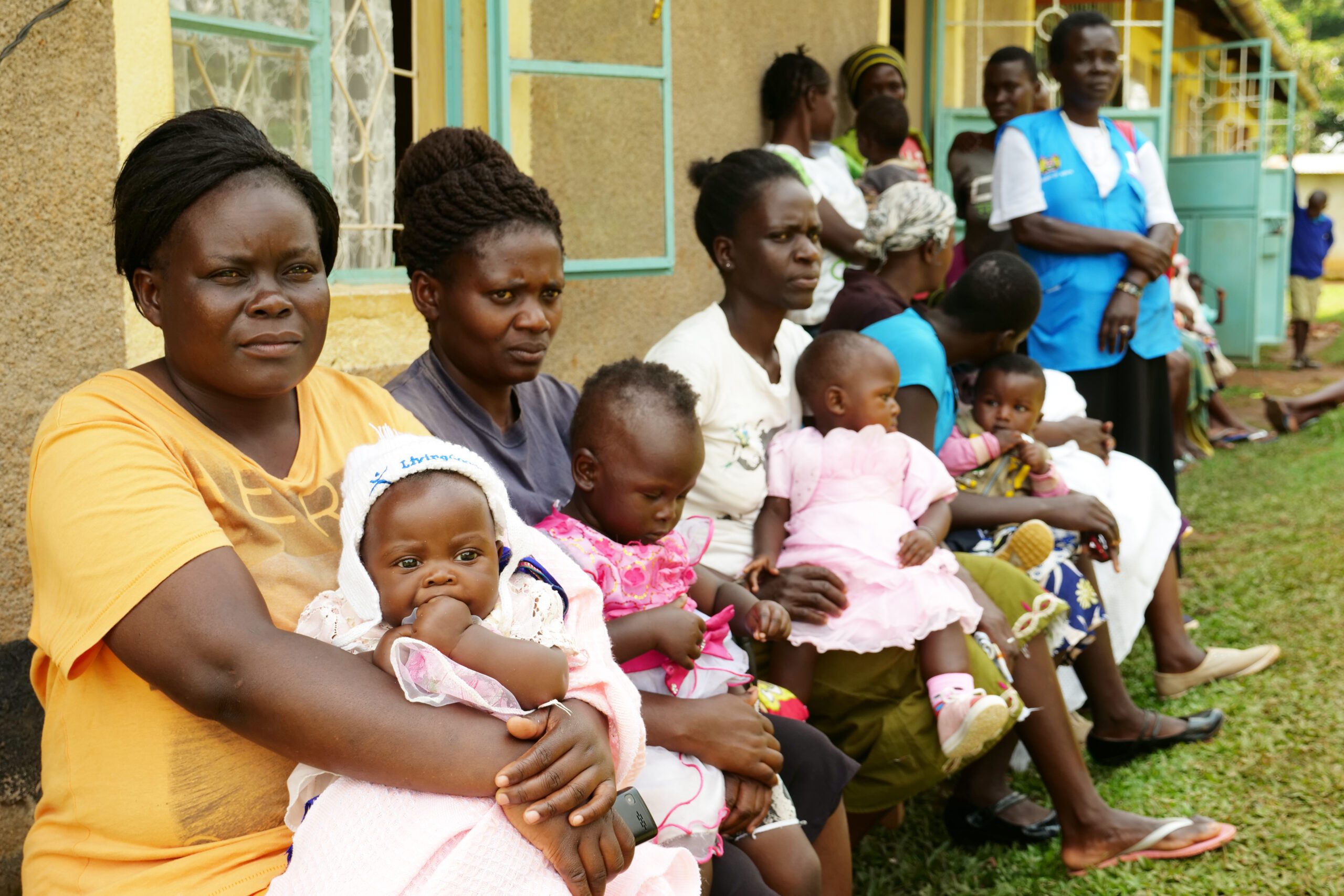 Women sit with their infants outside the Vikunga clinic, listening to speeches with potentially lifesaving messages during Maternity Open Day.