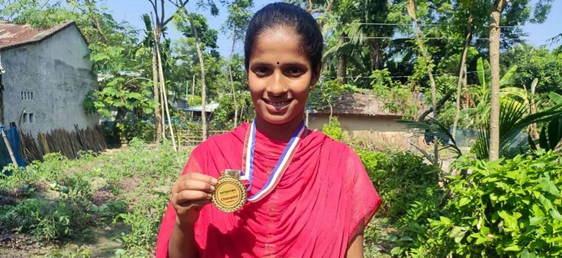 Mollika Biswas, 17-year-old farmer stands showing her 2022 International Nutrition Olympiad medal.