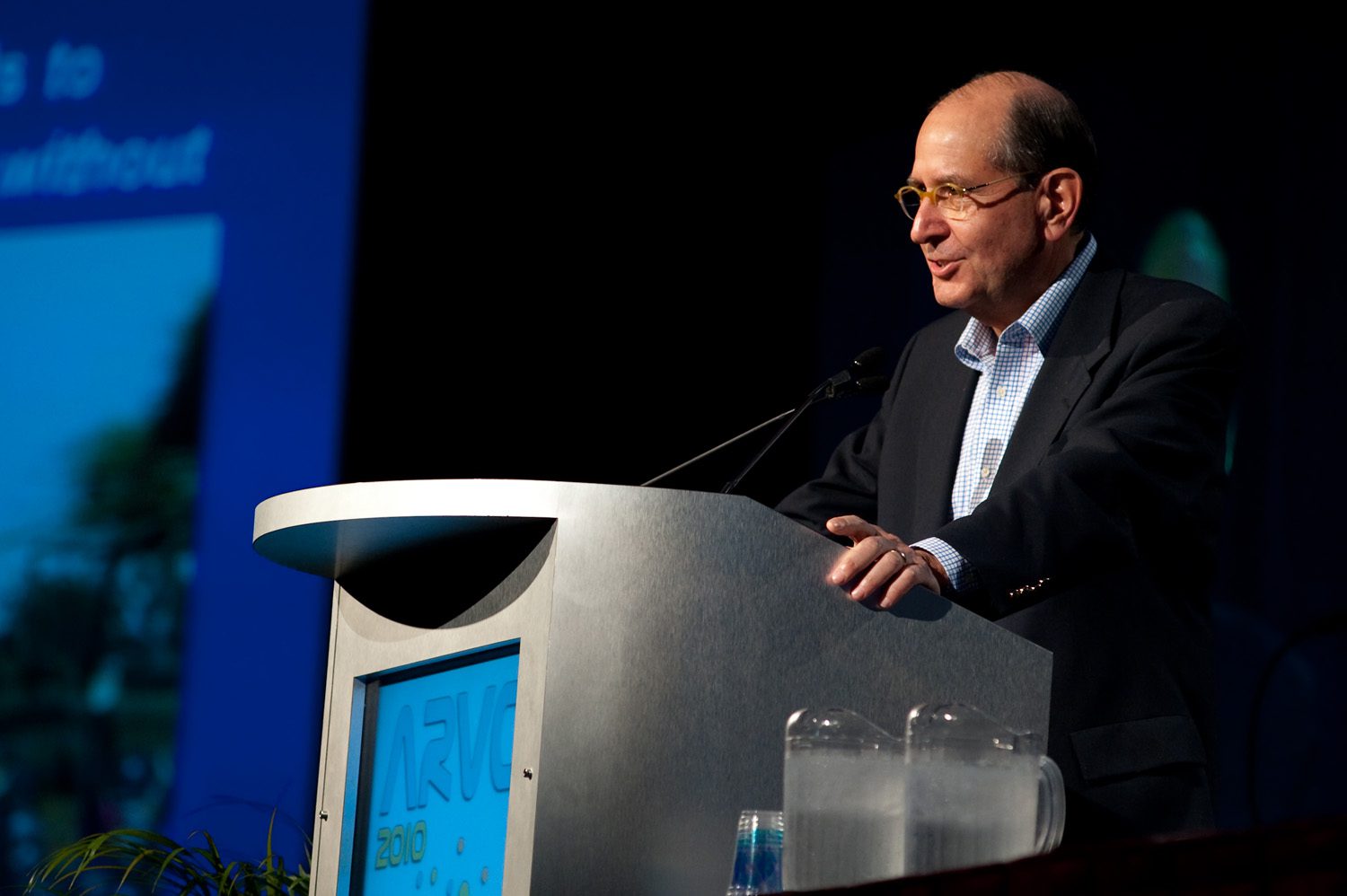 Professional man delivering speech at conference podium with microphone and water glasses.