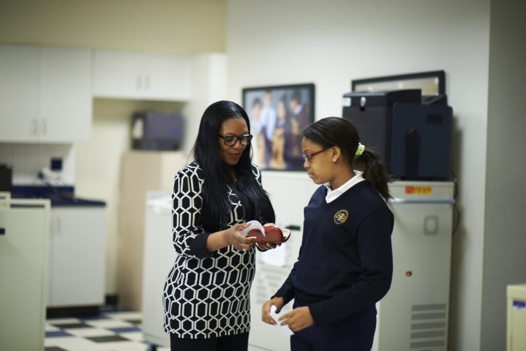 Female teacher wearing glasses in patterned dress talking to student also wearing glasses