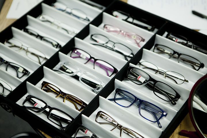 Multiple pairs of eyeglasses with different frame styles and colors neatly arranged in trays.