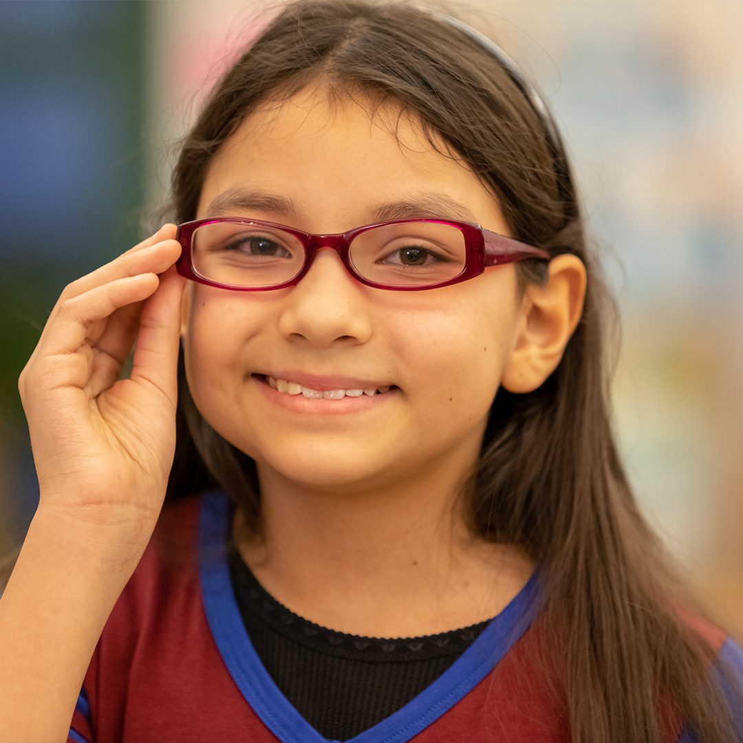A young school student from New York City smiles as she wears her new glasses.