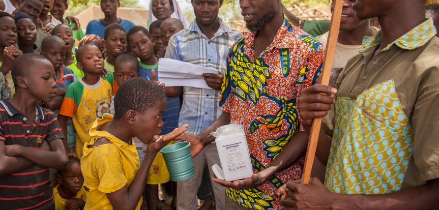 Man giving deworming medication to child with others in the background.