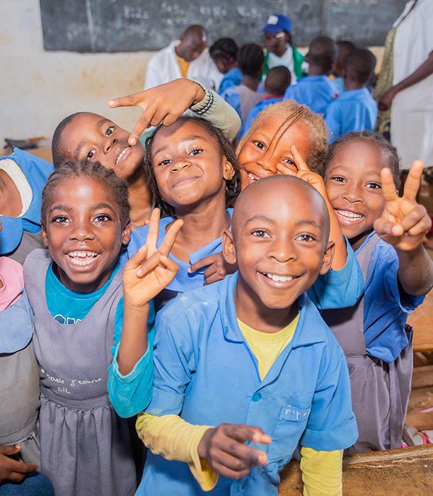 School children in Cameroon smiling at the camera doing the peace sign.