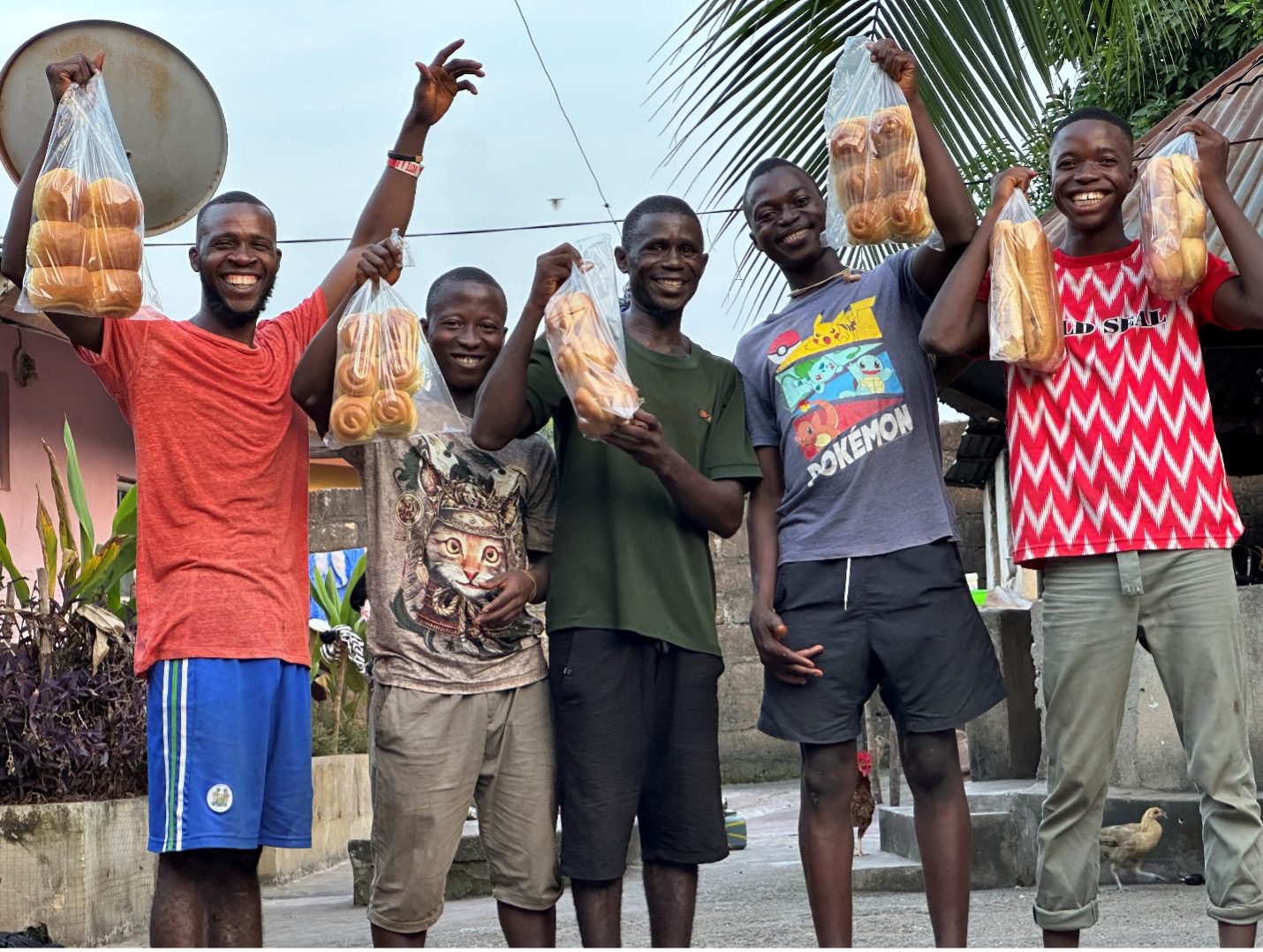 Five young men from Sierra Leone hold up bags of bread and rolls.