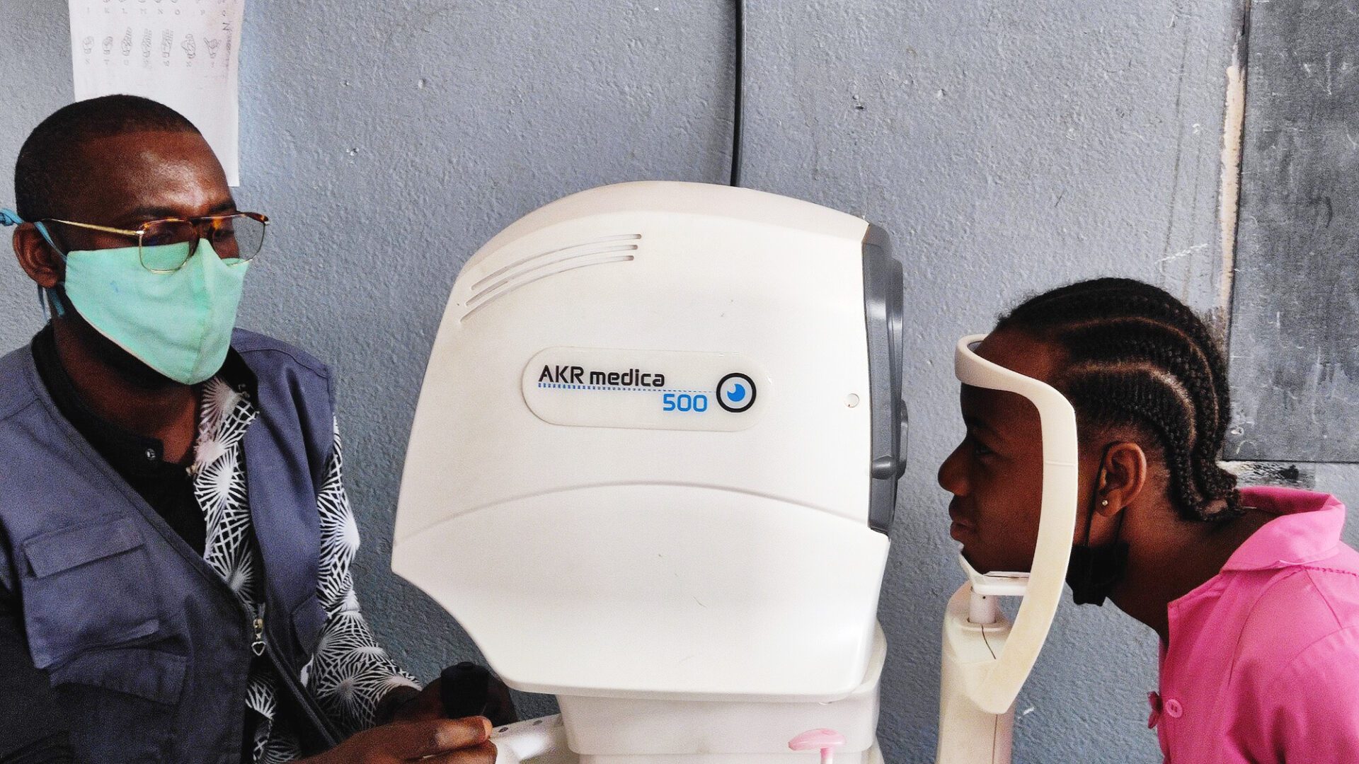 A health worker examines an adolescent boy's eyes using an autorefractor.