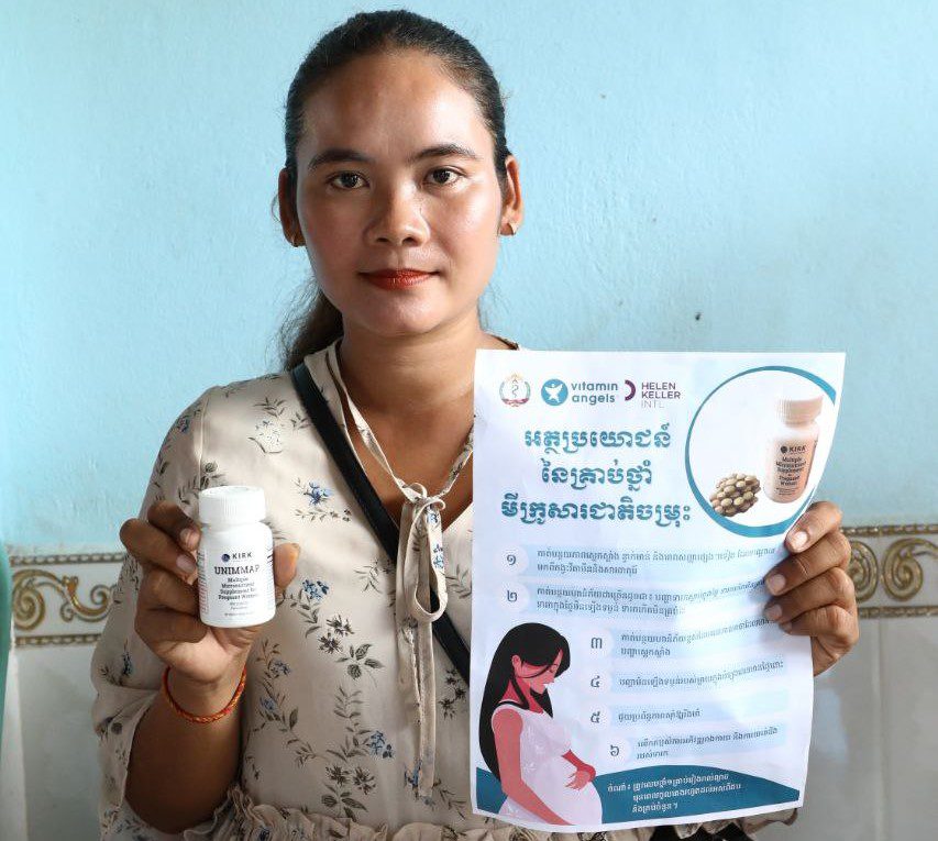 A Cambodian woman holds up a bottle of prenatal vitamins in one hand and a flyer about prenatal vitamins in the other.