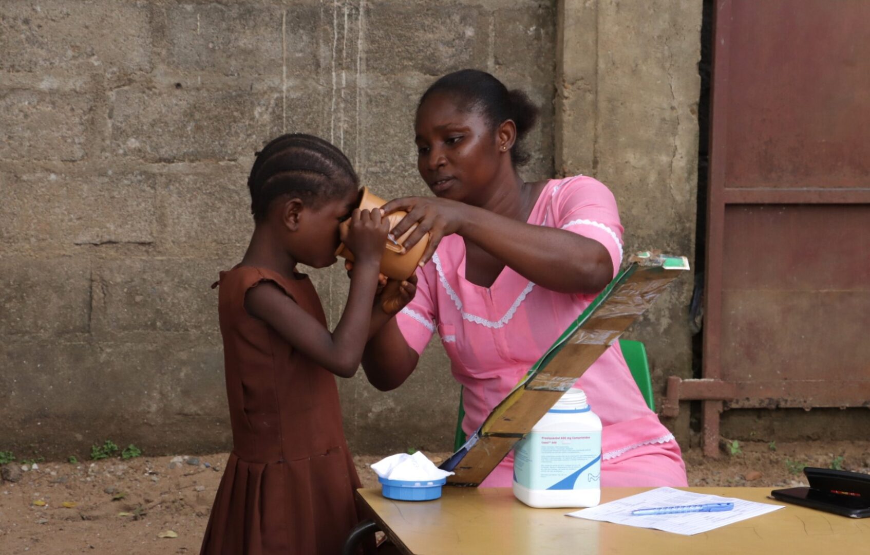 A female healthcare worker gives a young girl a drink of water.