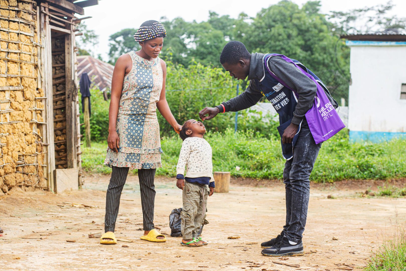 A community health worker in Cameroon gives a young boy a dose of vitamin A as his mother watches.
