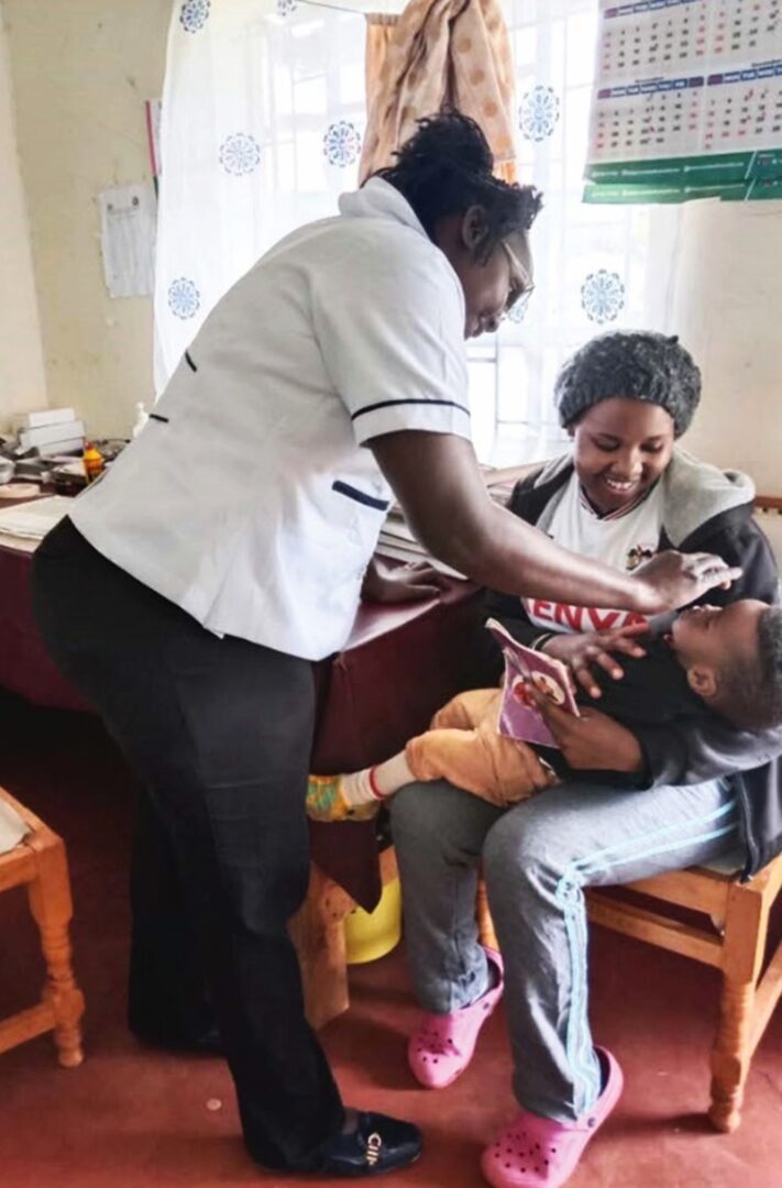 A Kenyan nurse gives a baby vitamin A as his mother holds him.