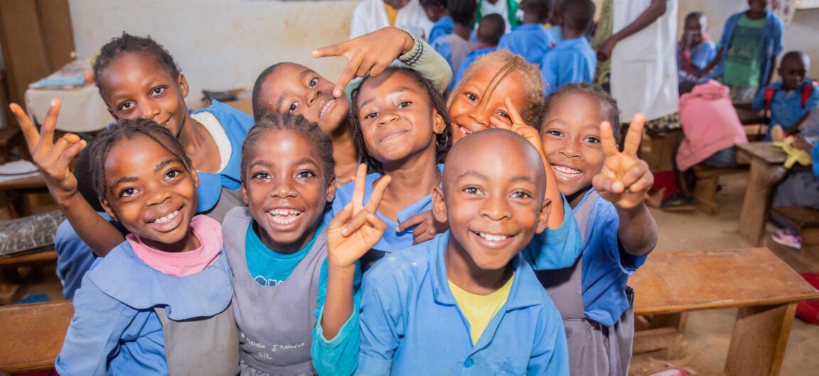 A group of school children in Cameroon smile for the camera.