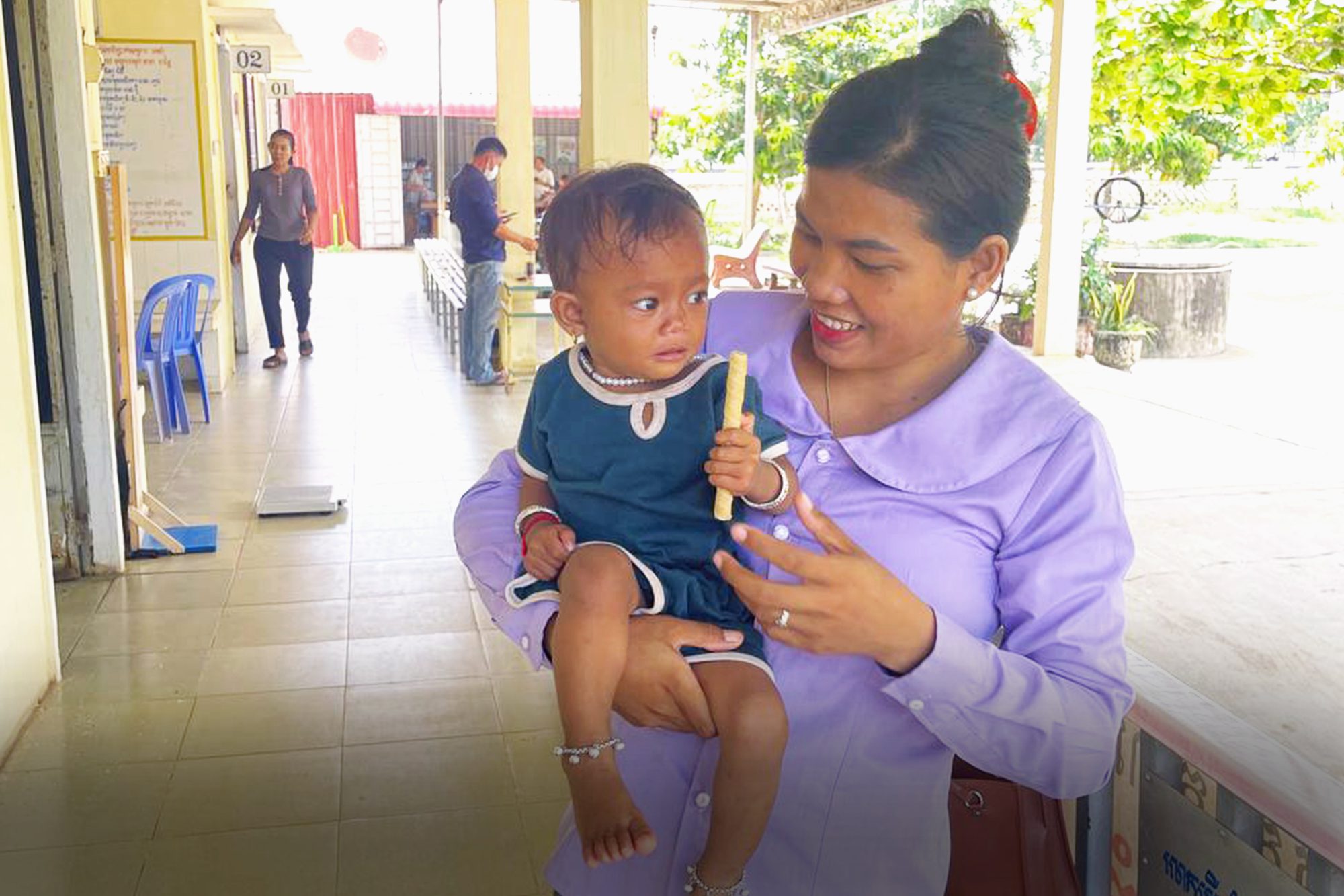Mother holding baby in Cambodia. Baby is holding a food supplement.