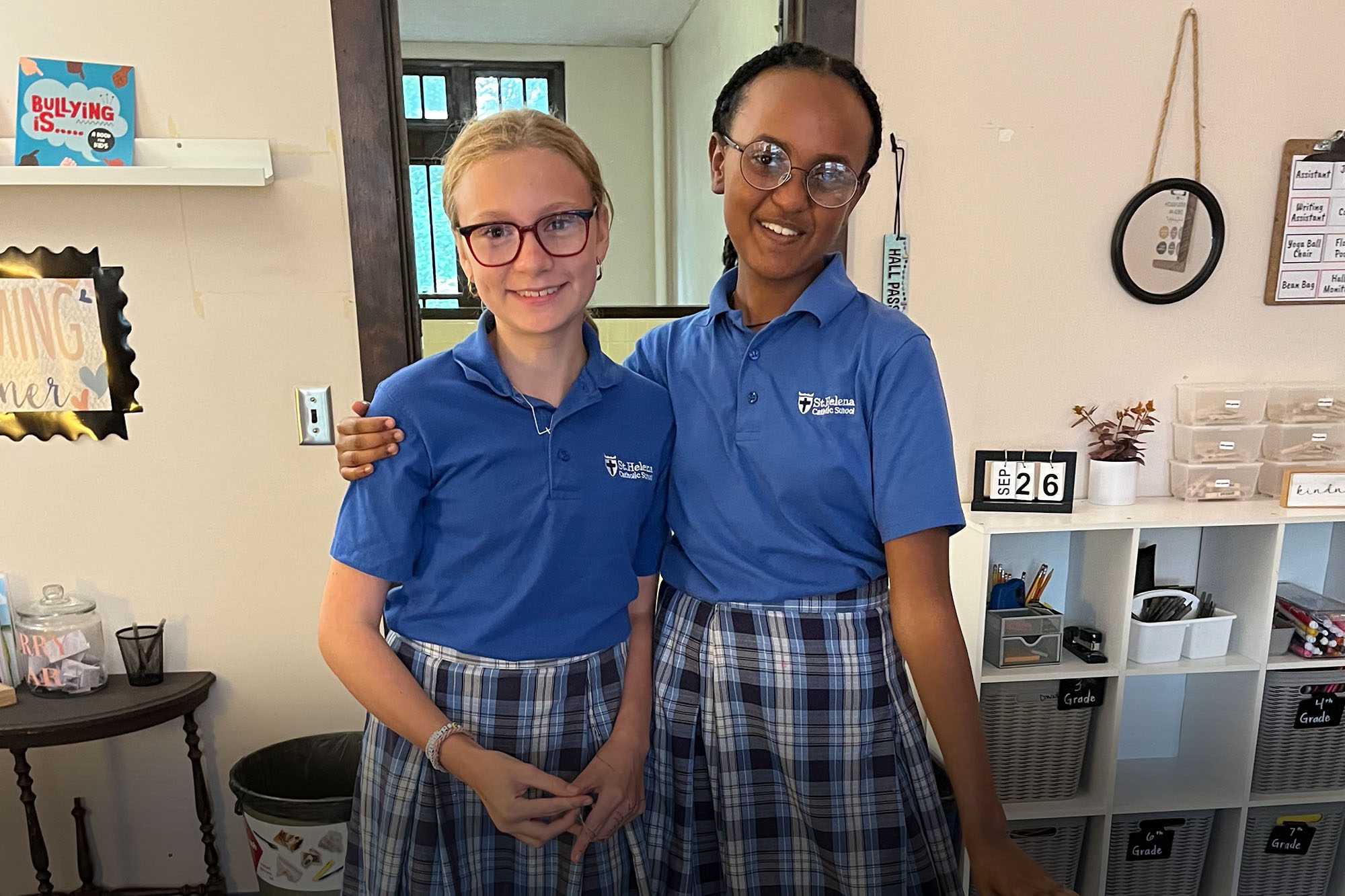 Two students one with their arm around the other smile joyously wearing new glasses they received.