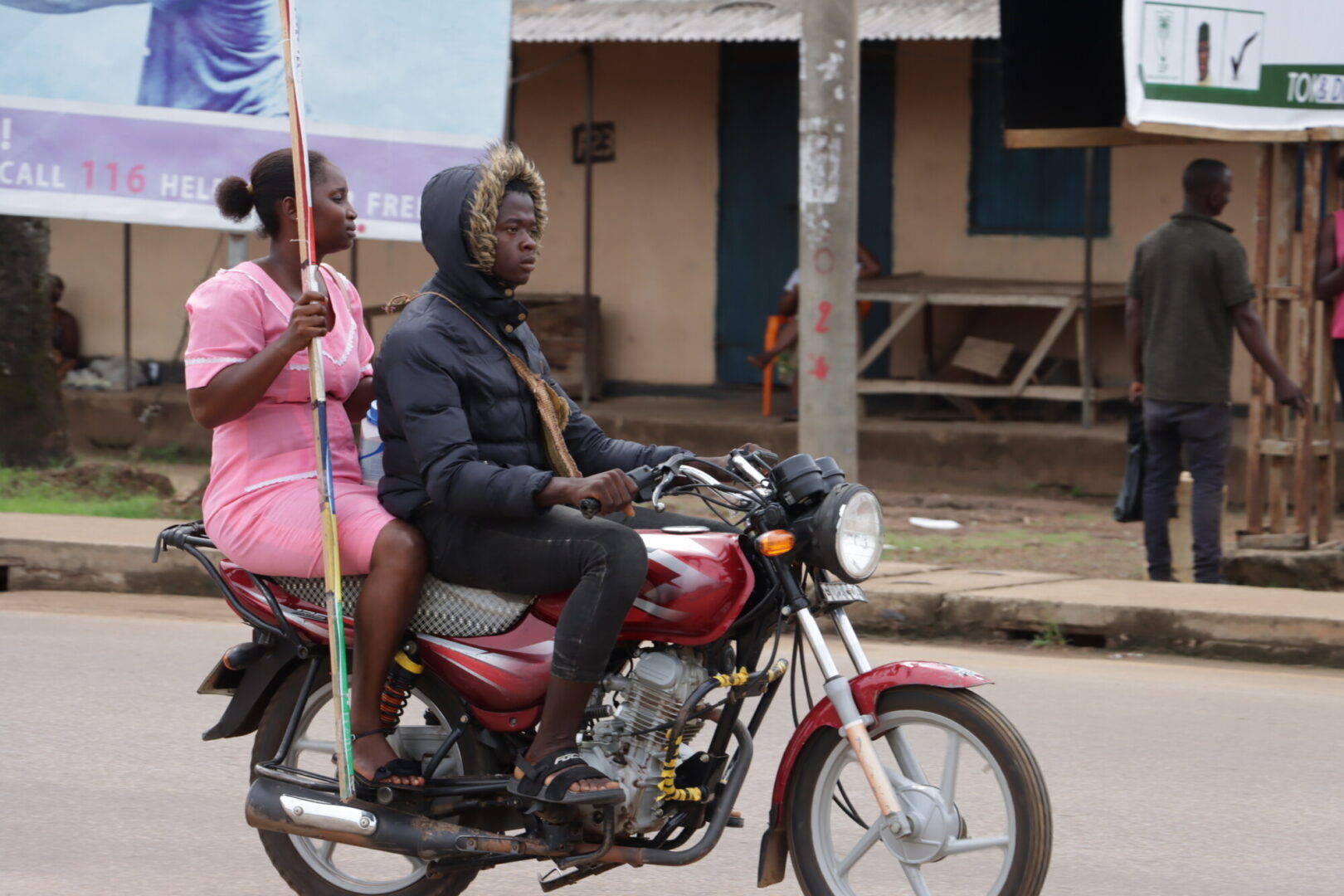 A female healthcare worker in Sierra Leone rides on the back of a motorbike.