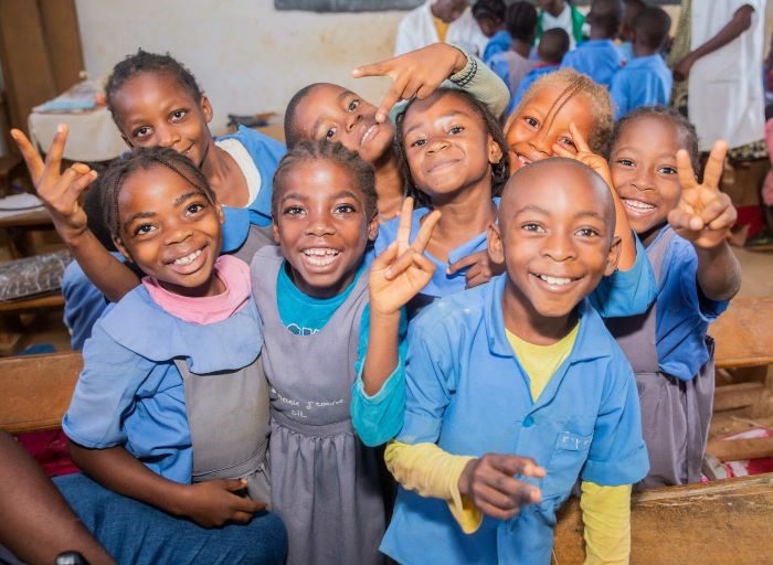 A group of boys and girls smile for the camera in a classroom in Cameroon.