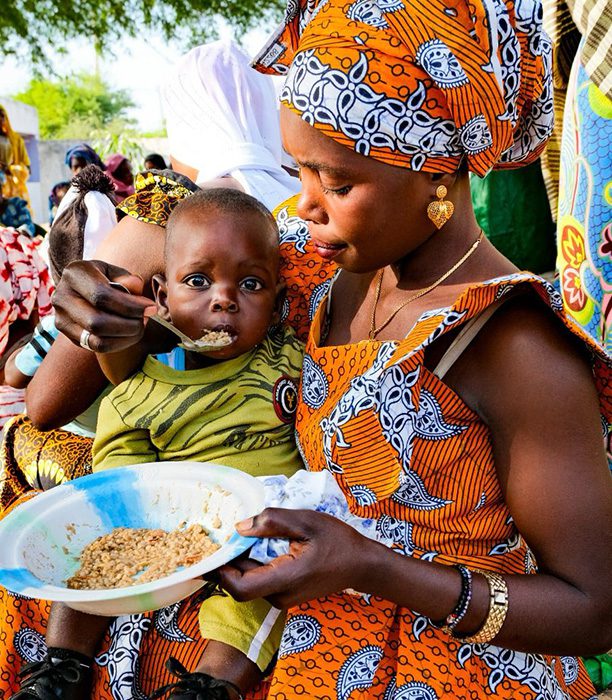 Senegalese child being fed porridge by his mother.