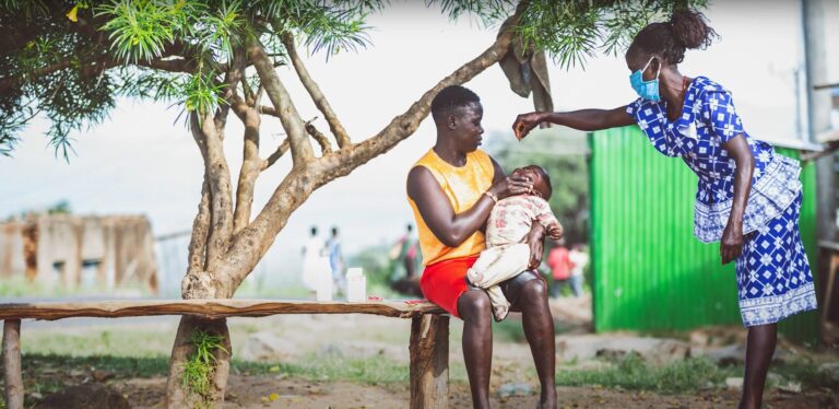 Woman giving Vitamin A to young child.