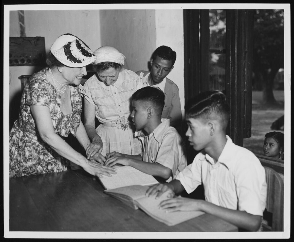Black and white photo of Helen Keller engaging with students.