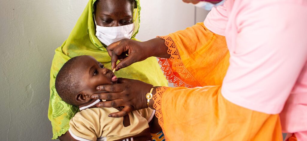 Healthcare worker administering vitamin A supplement to young child in clinic setting.