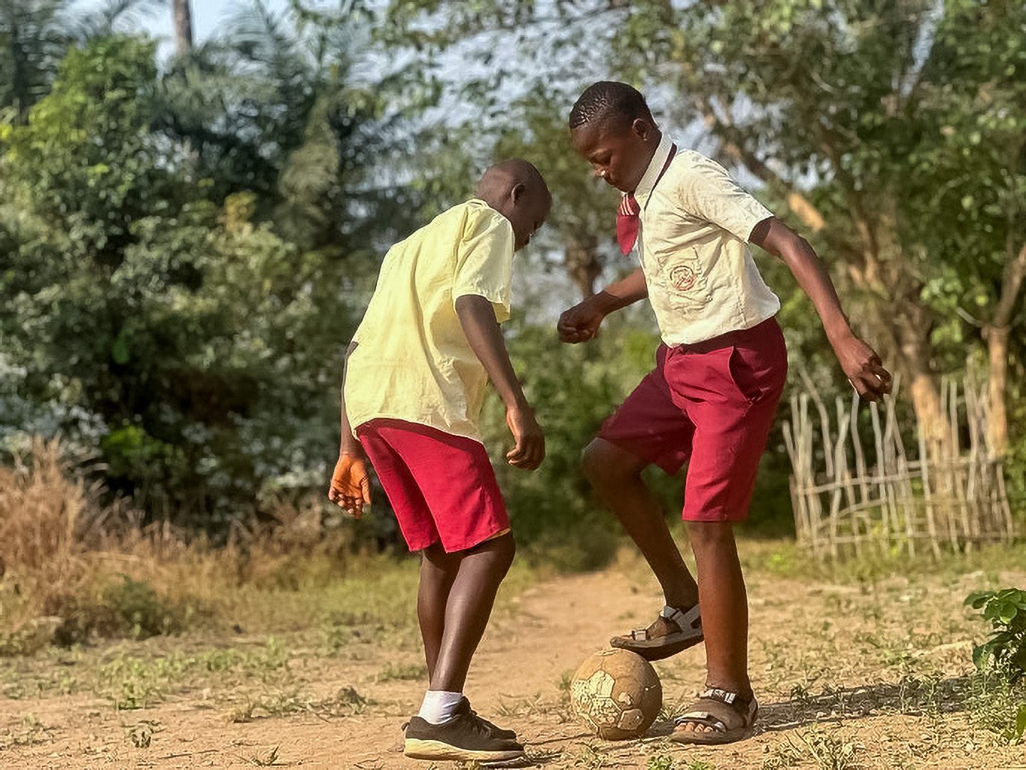 Two Sierra Leonean teenage boys play soccer together outside.