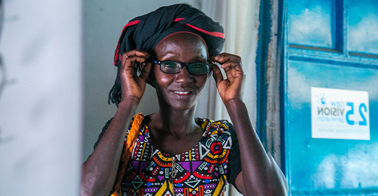 A woman fitting on her glasses through the mirror.