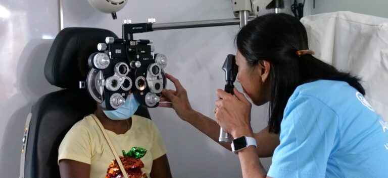 An eye doctor examines a girls' eyes with a phoropter.