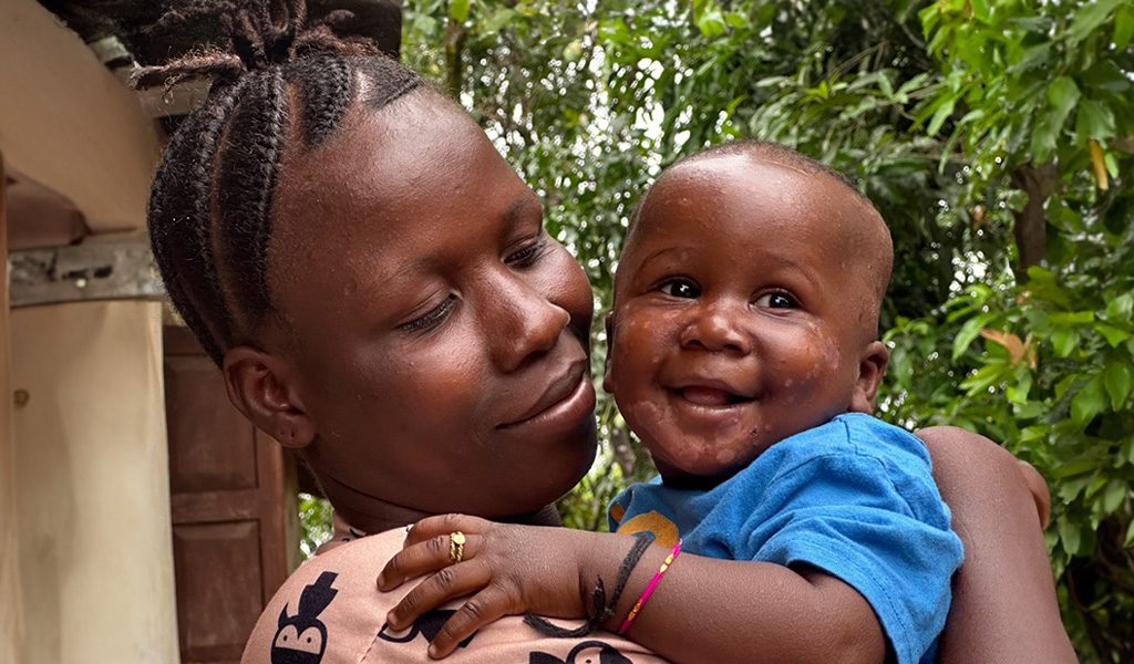 A mother, Kadiatu, lovingly holds her baby, Gabriel, in her arms, showcasing a tender moment of affection.
