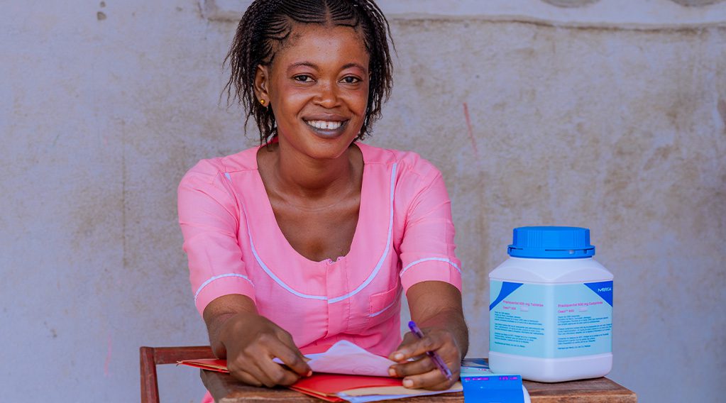 Helen Keller Intl trained healthcare worker smiles and looks at the camera with documents and medicine in front of her.