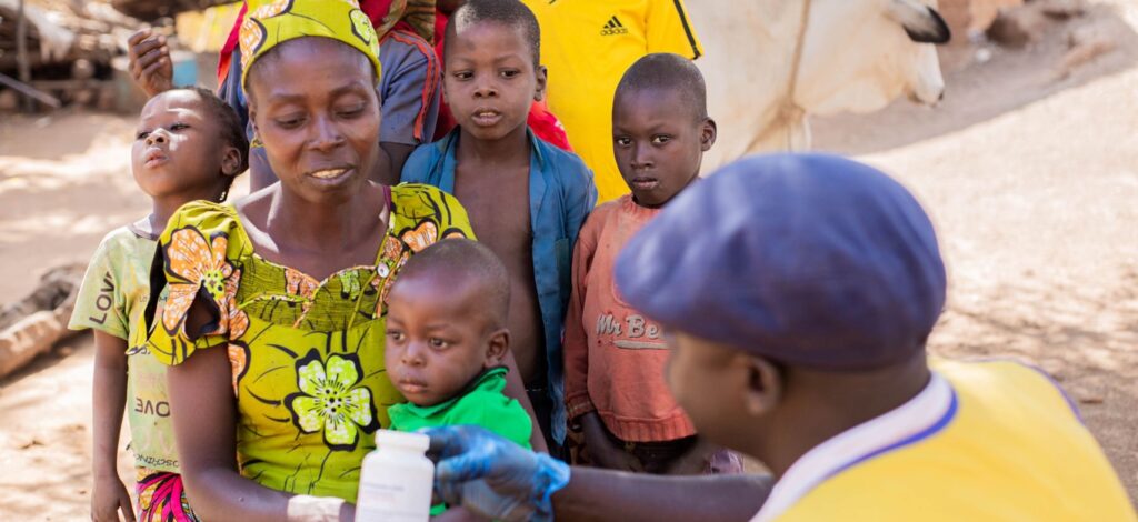 A Cameroonian community health worker shows a bottle if vitamin A to a mother and her children.