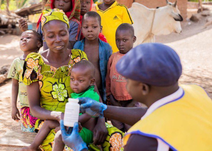 A Cameroonian community health worker shows a bottle if vitamin A to a mother and her children.