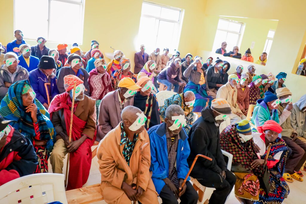 A large number of people sit in a room with bandages over their eyes after receiving cataract treatment. 