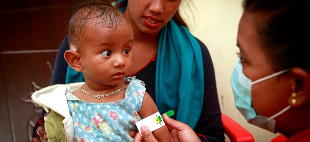 A young girl in Nepal has her arm measured by a healthcare worker.