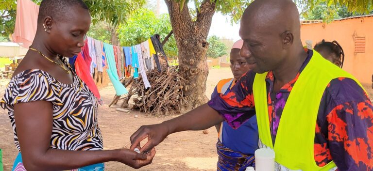 A man hands a woman pill while standing outside in Burkina Faso.