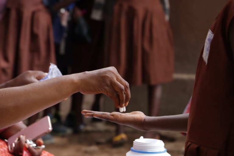A close up of a healthcare worker handing medication to a student.