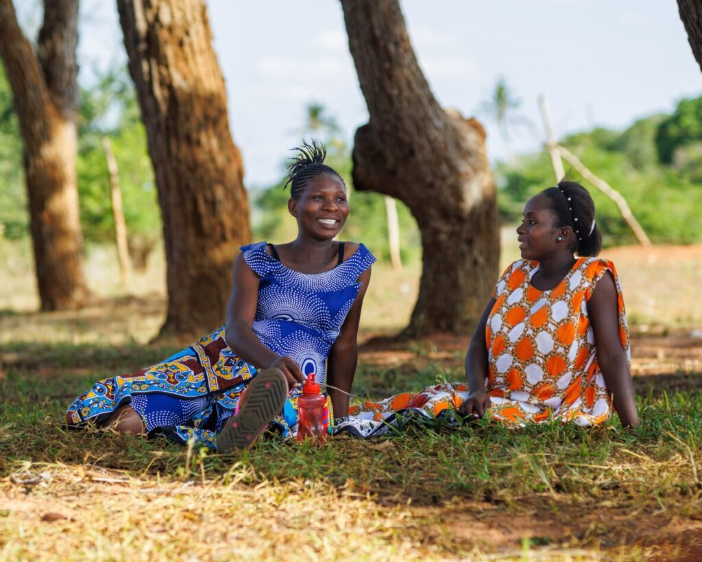Girls sitting on grass smiling together.