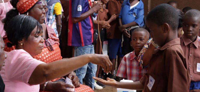 A woman hands a boy a pill.