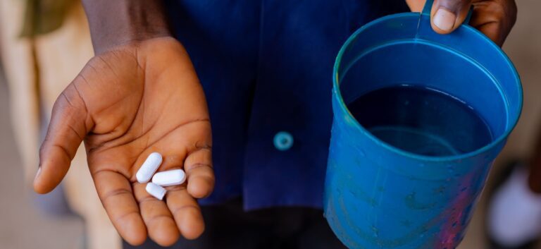 Hand showing medicine tablets with blue cup.
