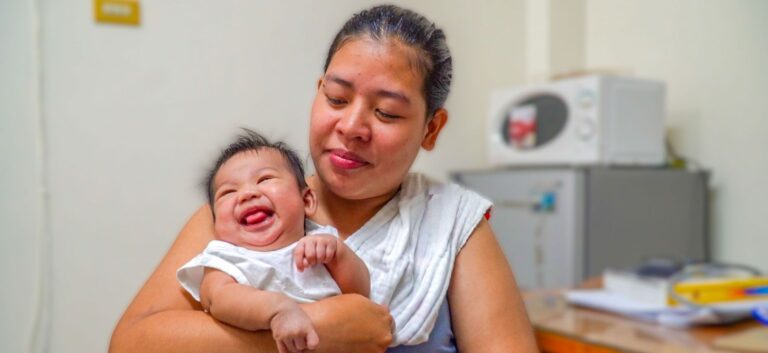 A woman in the Philippines holds a small baby while sitting in a medical office.