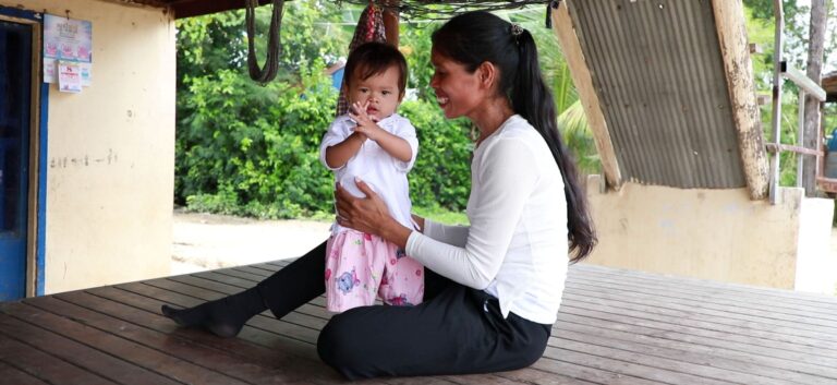 Mother holding toddler child on wooden porch in Cambodia.