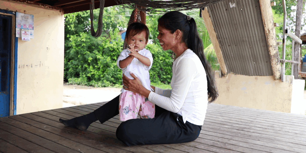 Mother holding toddler clapping hands outdoors in Cambodia.