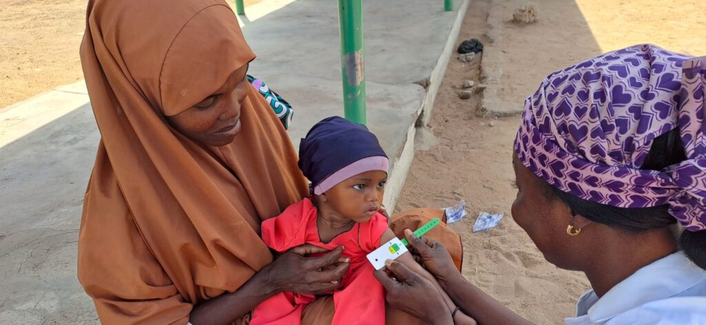 Health worker measuring a baby's arm circumference to screen for malnutrition in Nigeria.