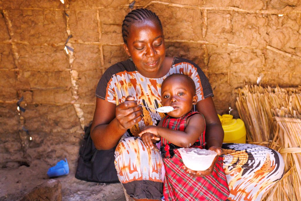Mother feeding toddler white porridge indoors