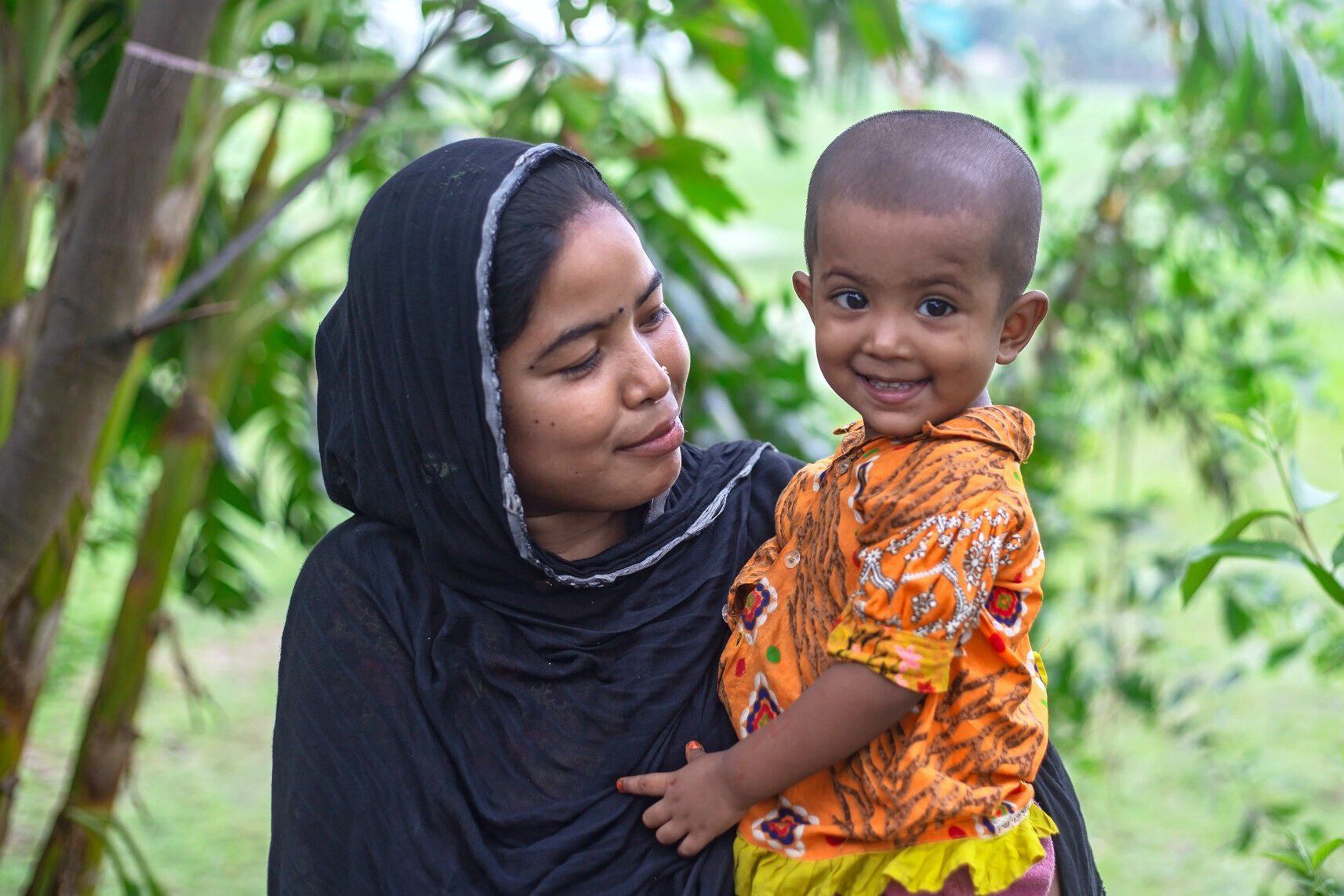 Woman holding smiling toddler in orange shirt