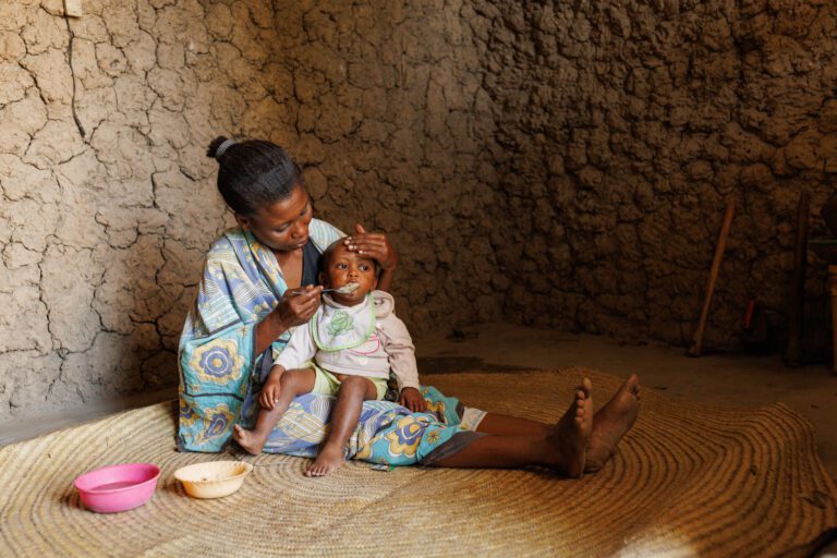 Mother feeding baby indoors on woven mat
