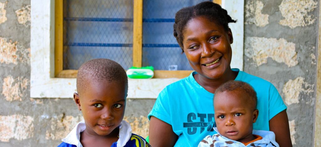 Mother holding baby with young boy outside house